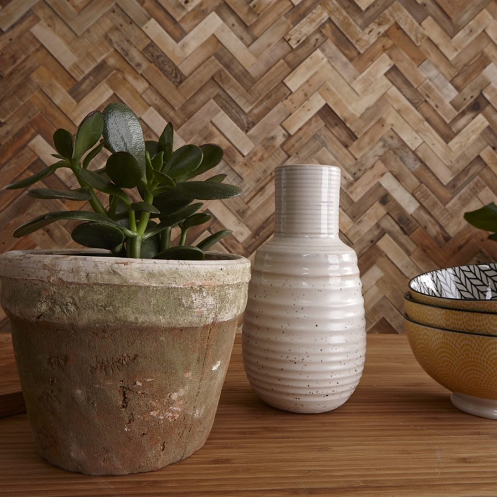 Panouri decorative din lemn reciclat Reclaimed - Herringbone, TimberWall, in fata carora se afla o masa cu vas decorativ alb, vas ceramic cu planta verde si trei boluri