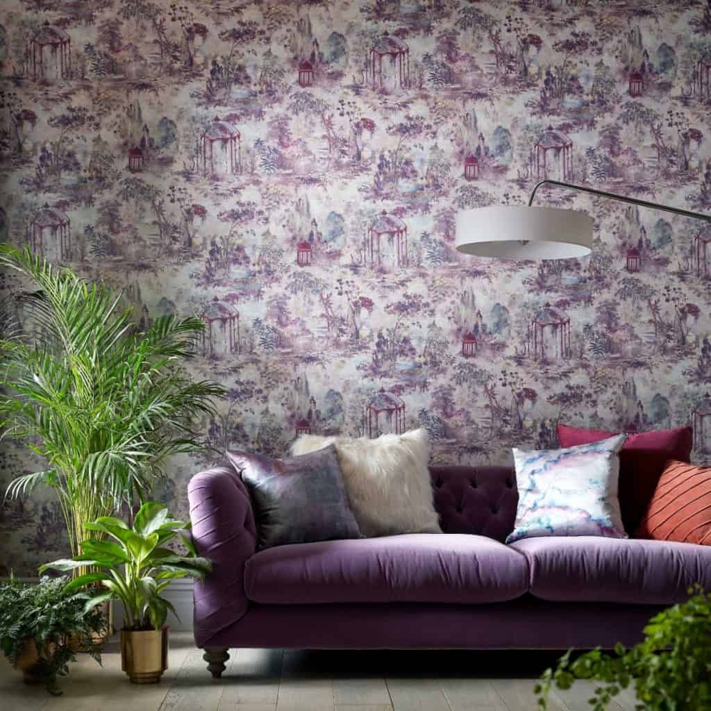 Tapet Pavilion, 1838 Wallcoverings, intr-un living cu canapea mov pe care se afla perne decorative, lampa suspendata alba si vase cu plante decorative