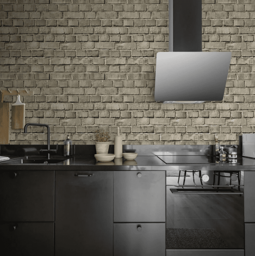 Tapet personalizabil Bricks, Sand, Rebel Walls, intr-o bucatarie cu hota si mobila neagra, cu plita si cuptor incorporate. Pe blatul negru se afla un set de vase bej